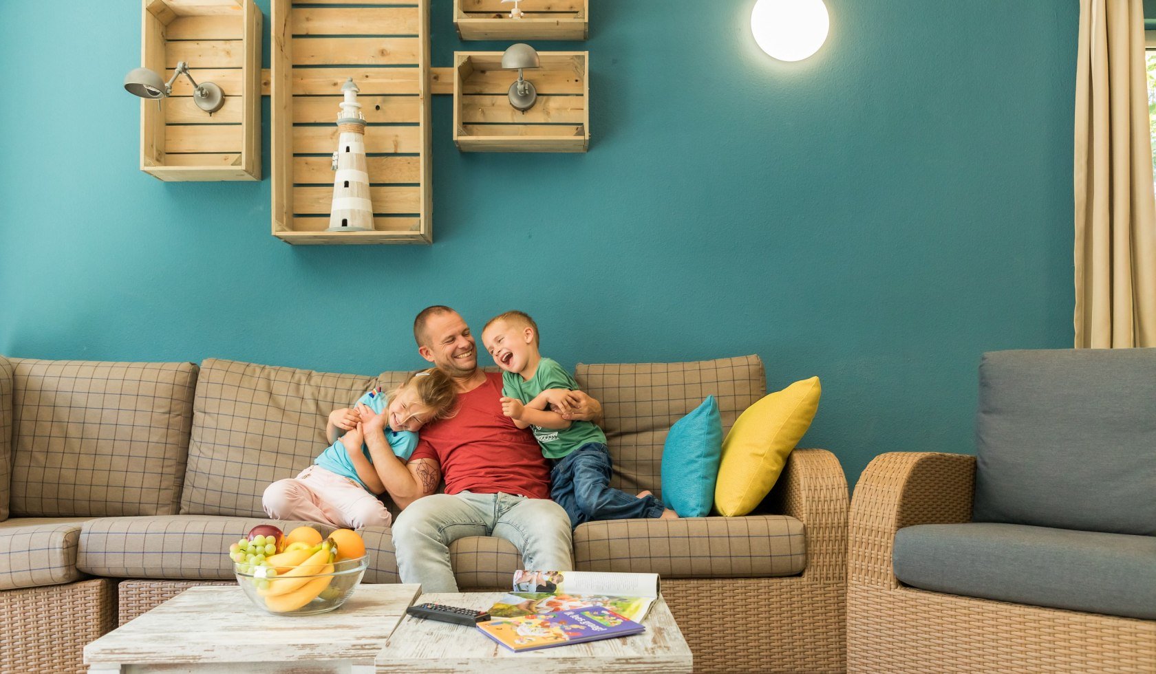 Father hugging his two children on the sofa in the holiday home., © Center Parcs